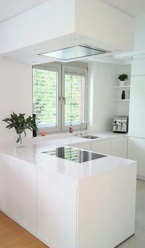 A white minimalist L shaped kitchen with a matching hood and a window and a view is very airy and welcoming