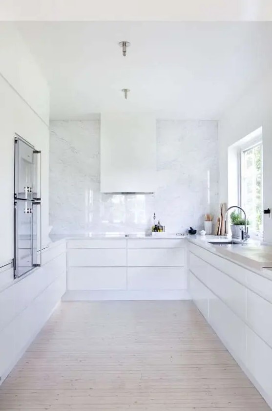 a white minimalist kitchen with a white stone backsplash plus countertops is a very airy and serene space