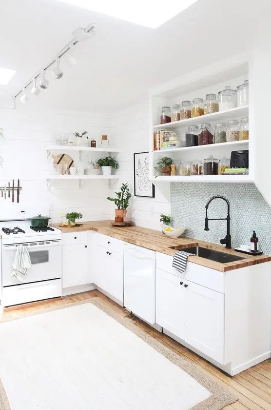 An L shaped kitchen in white, with butcherblock countertops and a skylight plus a blue penny tile backsplash
