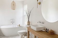 an airy Scandinavian bathroom with herrinbone tile, a wooden table as a vanity, a sink, a round mirror and lamps