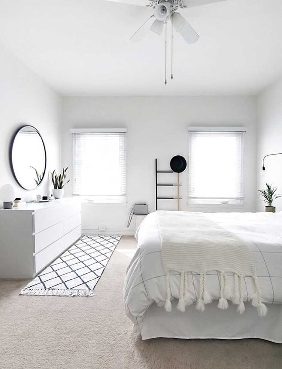 an airy Scandinavian bedroom with lot sof white, striped and tassel textiles, a black frame mirror, a sideboard