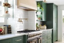 an elegant green kitchen with a blonde wood hood and a vintage cooker plus brass lamps and white countertops