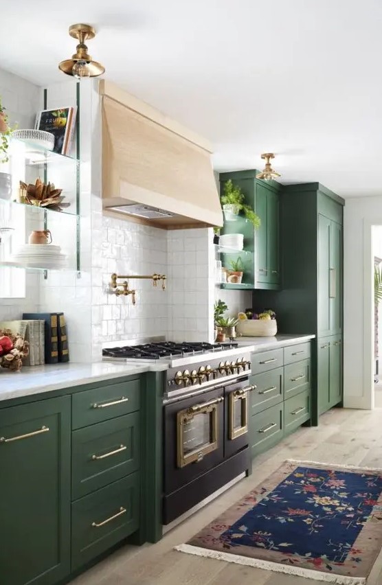 An elegant green kitchen with a blonde wood hood and a vintage cooker plus brass lamps and white countertops.
