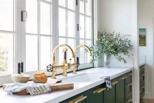 an elegant green one wall kitchen with a white stone countertop, windows as a backsplash and gold touches here and there
