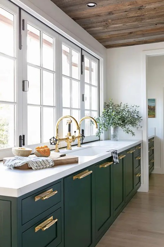 An elegant green one wall kitchen with a white stone countertop, windows as a backsplash and gold touches here and there.