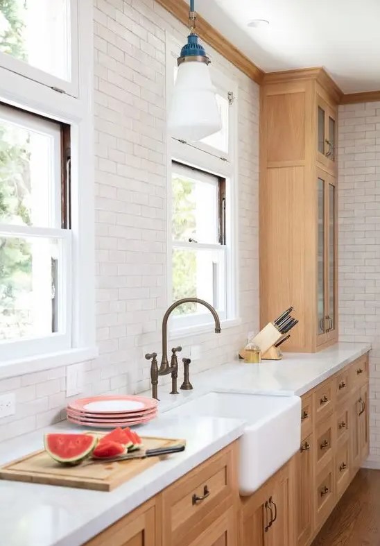 An elegant kitchen with light-stained shaker style cabinets, a white subway tile backsplash, white stone countertops.