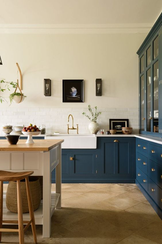 An elegant navy L shaped kitchen with shaker style cabinets, a white kitchen island and table, a gallery wall and some decor