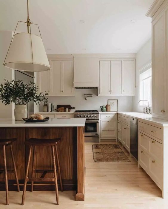 An elegant neutral L shaped kitchen with shaker cabinets, white stone countertops, a stained kitchen island, stained stools and a pendant lamp