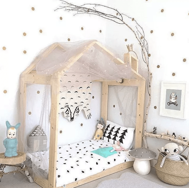 an ethereal Scandinavian kids' room with a wooden house shaped bed, a branch shelf, polka dot walls, artworks and some fun toys