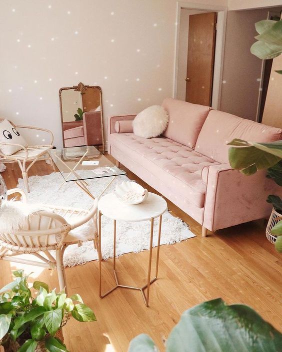 a soft-colored living room with neutral walls, a pink sofa, rattan chairs, refined tables and a mirror in a chic frame