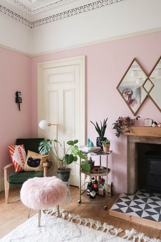 a pink living room with chic modern furniture, a fireplace clad with tiles, lots of potted plants and printed pillows