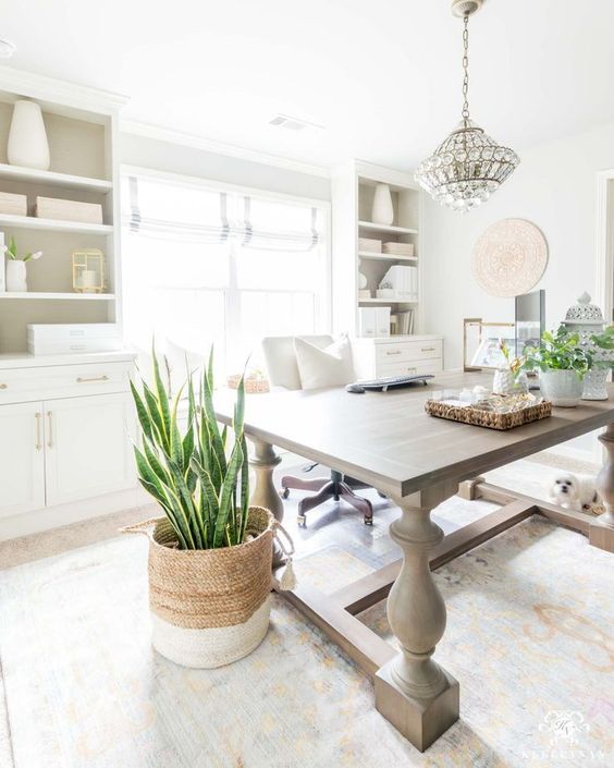 23 a neutral farmhouse home office with white furniture, a large table, a crystal chandelier and lots of potted greenery is very chic