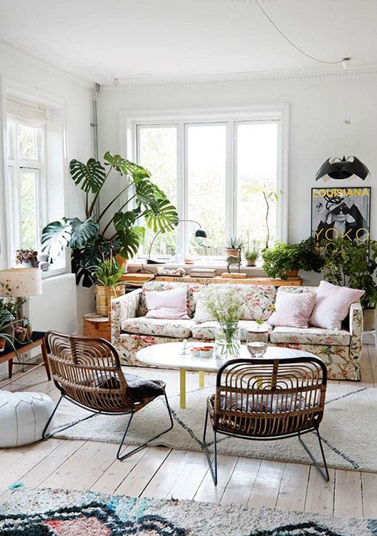 a boho living room in neutrals, with a floral sofa, rattan chairs, potted greenery and a printed rug