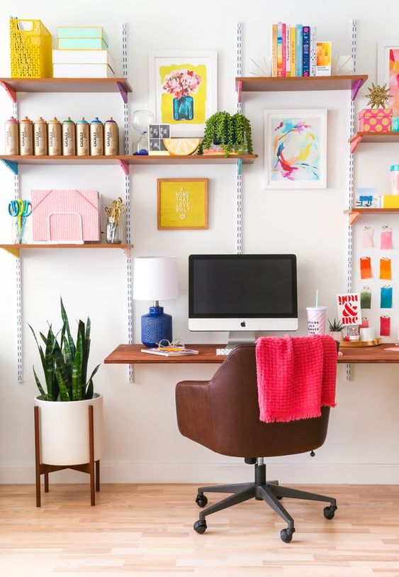a fun home office with open shelves and colorful artworks and stickers feel very spring or summer like