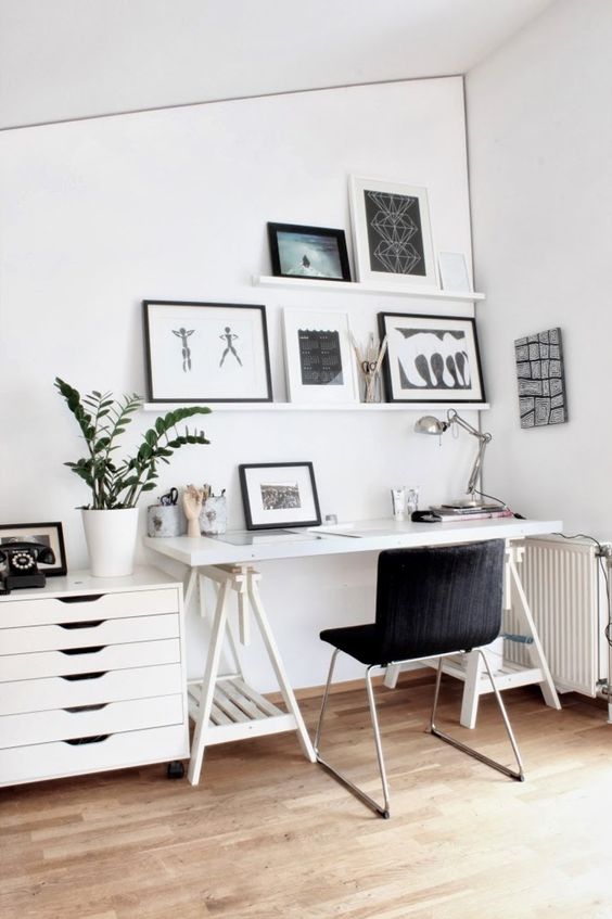 a Scandinavian home office with a white trestle desk, a black chair, a cabinet, ledges with black and white artworks