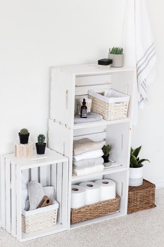 a bathroom shelving unit of white crates, with baskets and boxes, with towels, cacti and toilet paper is very stylish