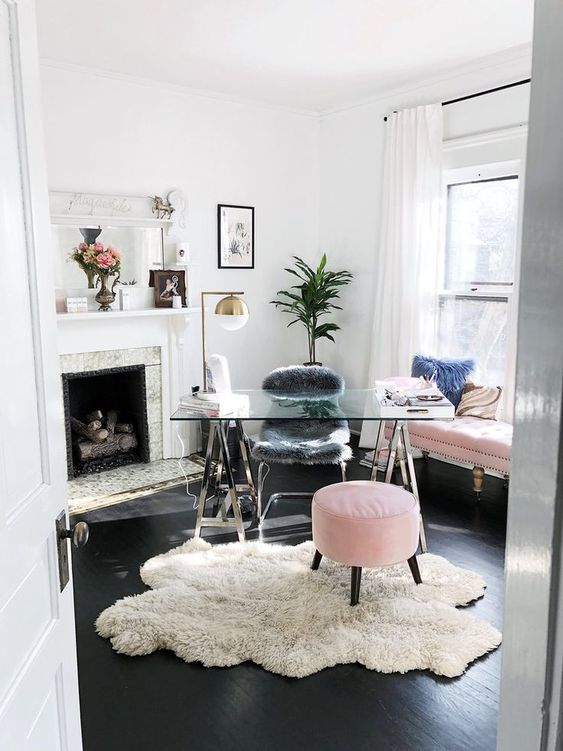 a glam home office with a glass and metal trestle desk, a pink sofa and ottoman, a fur chair and a fireplace is amazing