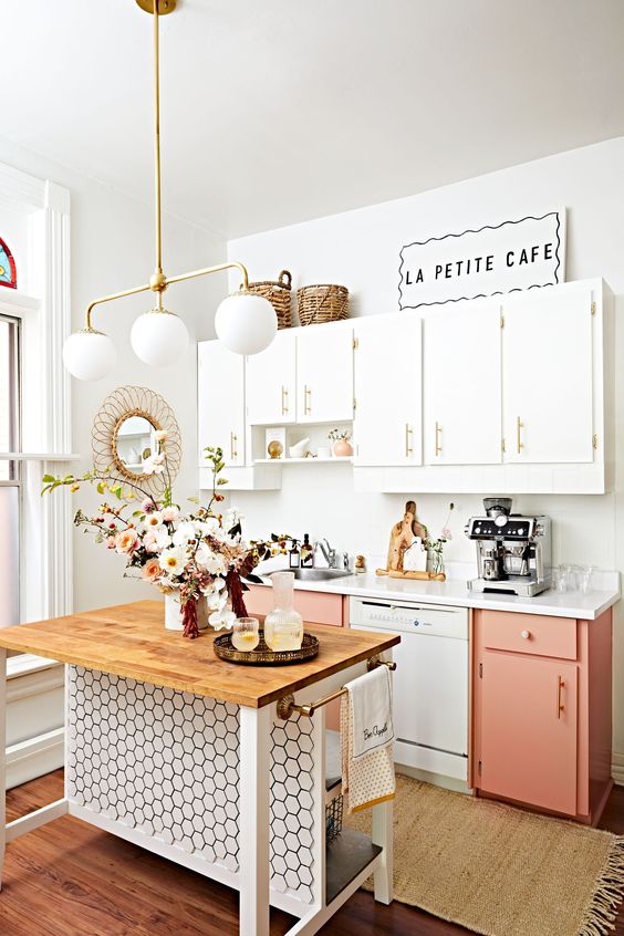 a little cozy bistro kitchen with white and pink cabinets, a small kitchen island clad with tiles and a pretty retro pendant lamp