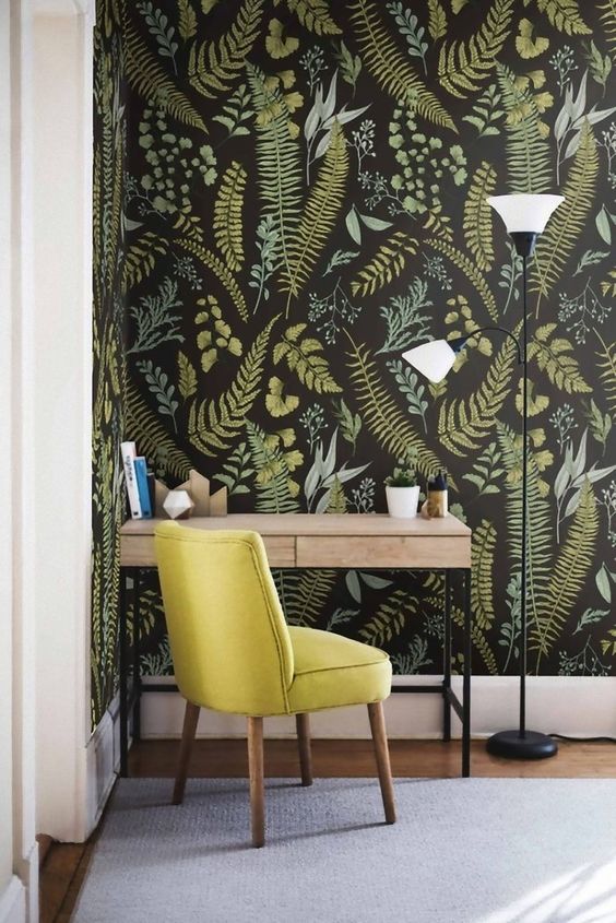a mid-century modern workspace with moody botanical wallpaer, a wooden desk, a mustard chair and a cool floor lamp next to the table