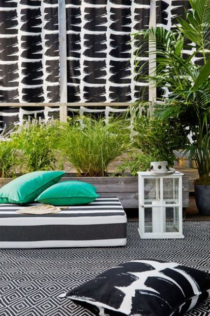 a modern monochromatic terrace with a striped mattress, printed textiles, a candle lantern and potted greenery