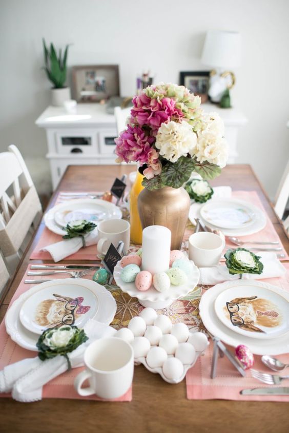 a pretty small Easter tablescape with pink placemats, a bold floral centerpiece, candles and pastel eggs plus bunny print plates