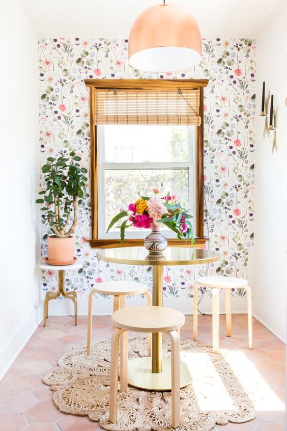 a small dining nook with a watercolor floral wallpaper wlal, a round table and some stools and a pink suspended lamp