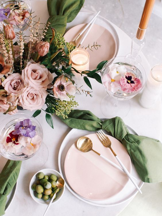 a spring table setting with pink florals, white and pink plates, green napkins, candles and floral cocktails