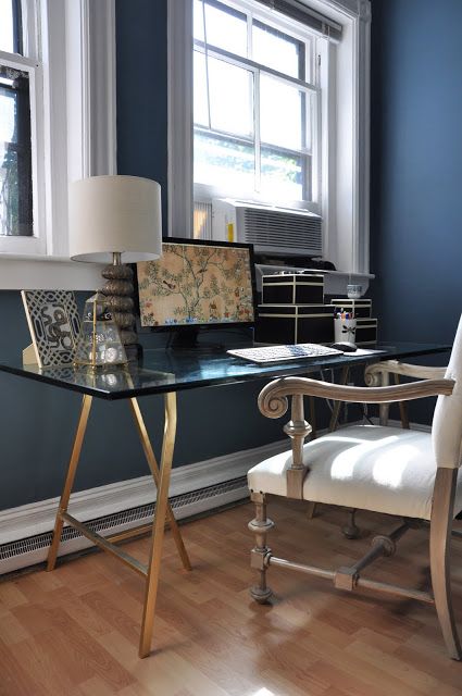 a vintage-inspired home office with navy walls, a refined glass and metal trestle desk, a vintage chair and a table lamp