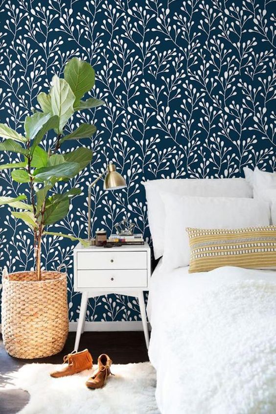 a welcoming bedroom with navy and white botanical wallpaper, white furniture, a potted plant and some pretty textiles