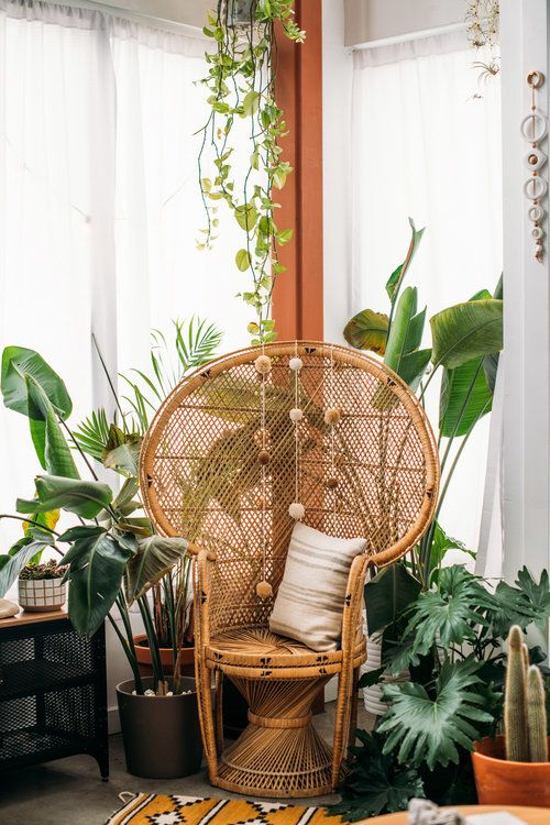 a lovely boho nook with potted plants, a peacock chair, a pillow and pompoms plus a bright boho rug