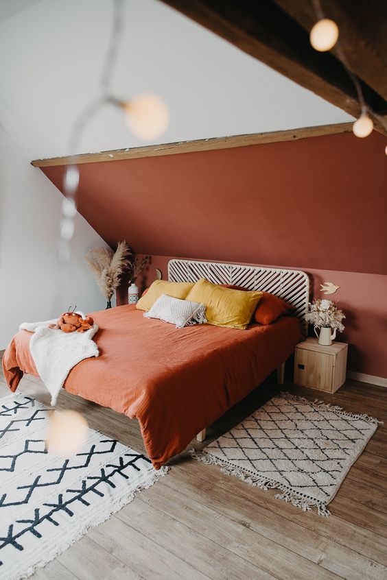 a lovely attic bedroom with a terracotta accent wall, a pretty bed and terracotta bedding, wooden nightstands and lights