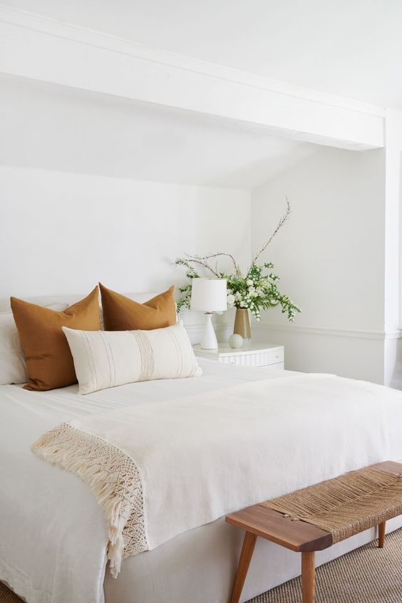 a lovely neutral bedroom with a white bed, chic white bedding, a wood and twine bench for a slight rustic feel