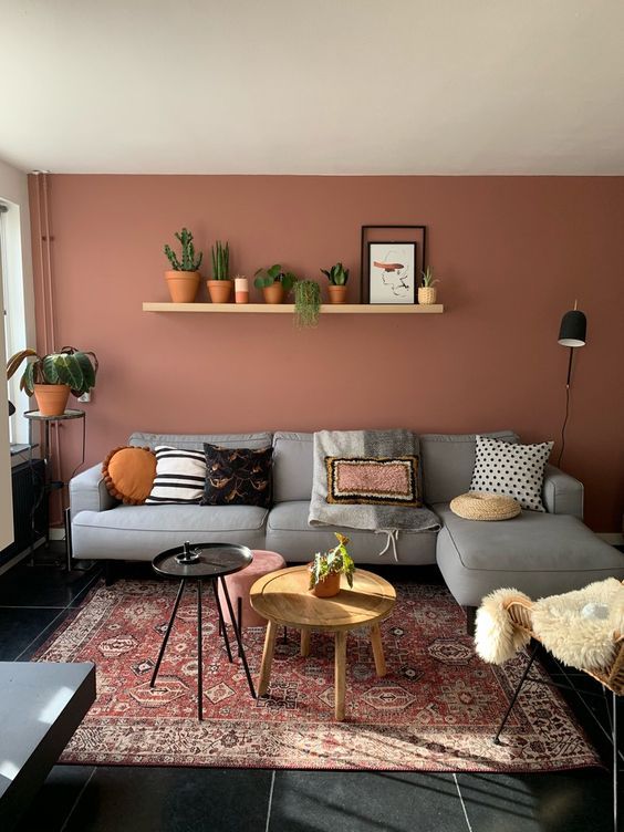 14 a pretty boho living room with a terracotta statement wall, a grey sectional, a rattan chair and some potted plants and round tables