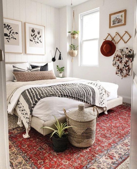 a neutral boho bedroom with an upholstered bed, potted plants, a gallery wall and a basket plus a plant at the foot