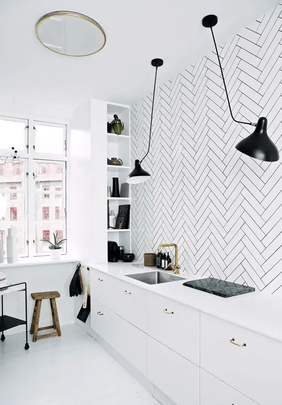 a Scandinavian kitchen with sleek white lower cabinets, a white herringbone tile backsplash, shelves, black lamps and a wooden stool