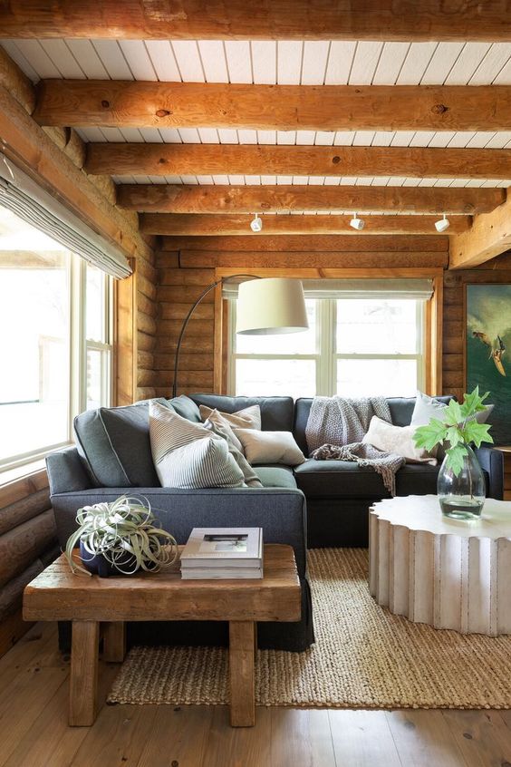 a chalet living room with a grey sectional sofa, a stone table, a wooden side table and wooden beams