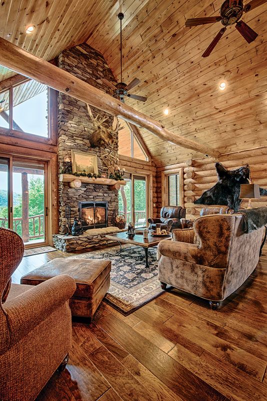 a chalet living room with wooden walls, a floor and a ceiling, a stone clad fireplace, leather and fabric upolstered furniture and taxidermy