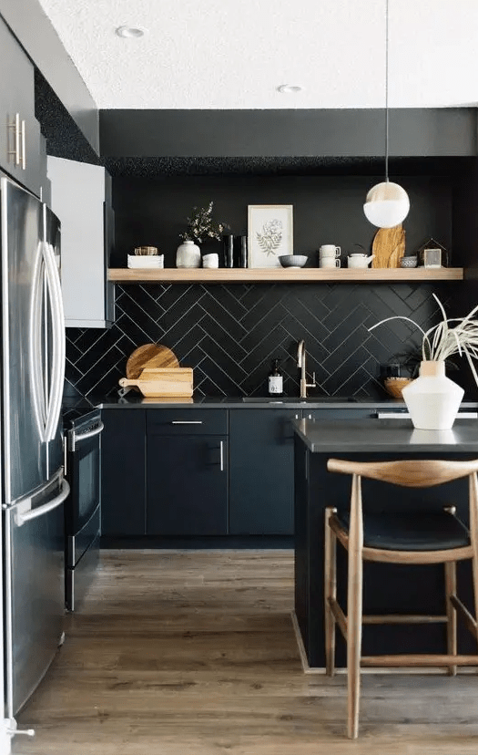 a chic black kitchen with black cabinets, a tile backsplash, concrete countertops and touches of light colored wood