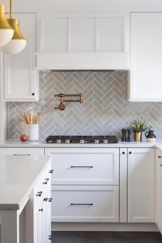 a chic white farmhouse kitchen with a grey herringbone backsplash and white countertops plus gold and brass touches