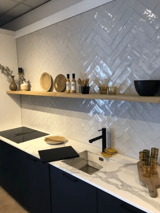 a contemporary black kitchen with white stone countertops, a white herringbone backsplash, an open shelf and a black faucet
