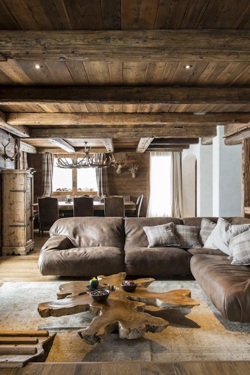 a cozy chalet living room clad with wood, with a large leather sofa, a wood slice table and some antlers