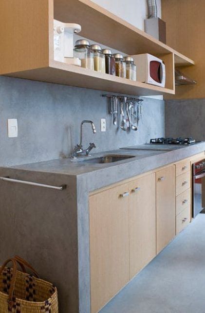 a light stained kitchen with a concrete backsplash and countertops plus stainless steel handles is a laconic and cool idea