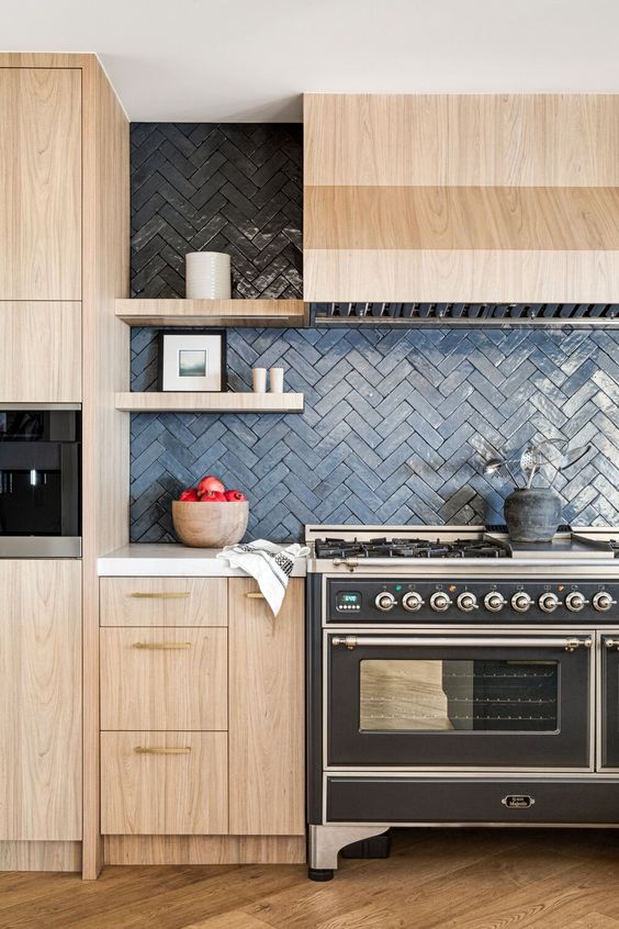 a light-stained kitchen with a lovely matte navy herringbone tile backsplash, white countertops and built-in appliances