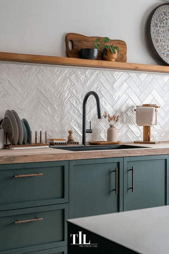 a modern kitchen with dark green cabinets, butcherblock countertops, a white herringbone tile backsplash, an open shelf