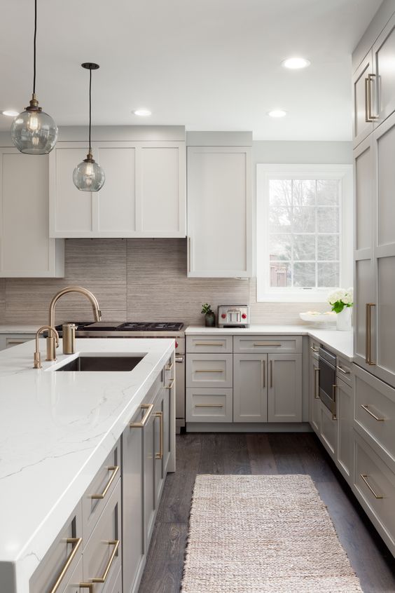 a modern light grye kitchen with white quartz countertops, brass touches, a wood tile backsplash and glass pendant lamps