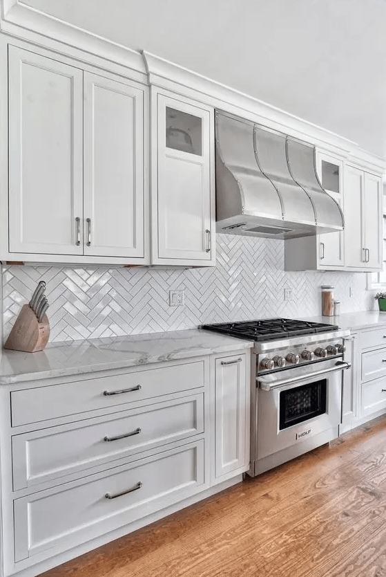 a neutral farmhouse kitchen with shaker cabinets, a herringbone tile backsplash, stone countertops and stainless steel appliances