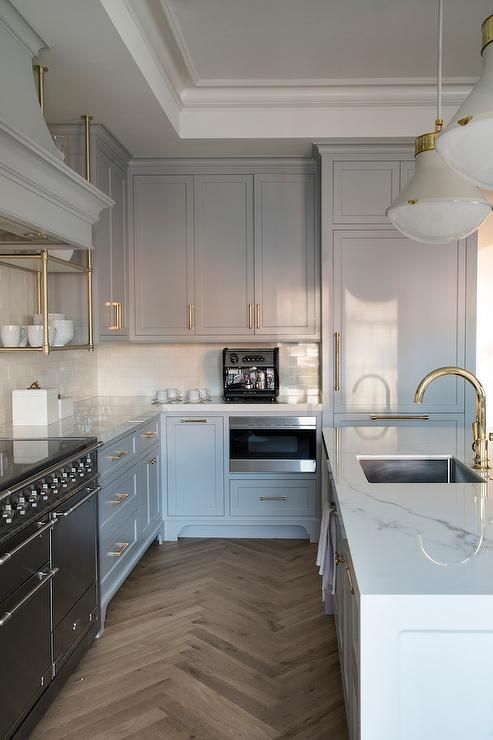a refined grey kitchen with a white tile backsplash and grey quartz countertops plus touches of gold and elegant lamps over the island