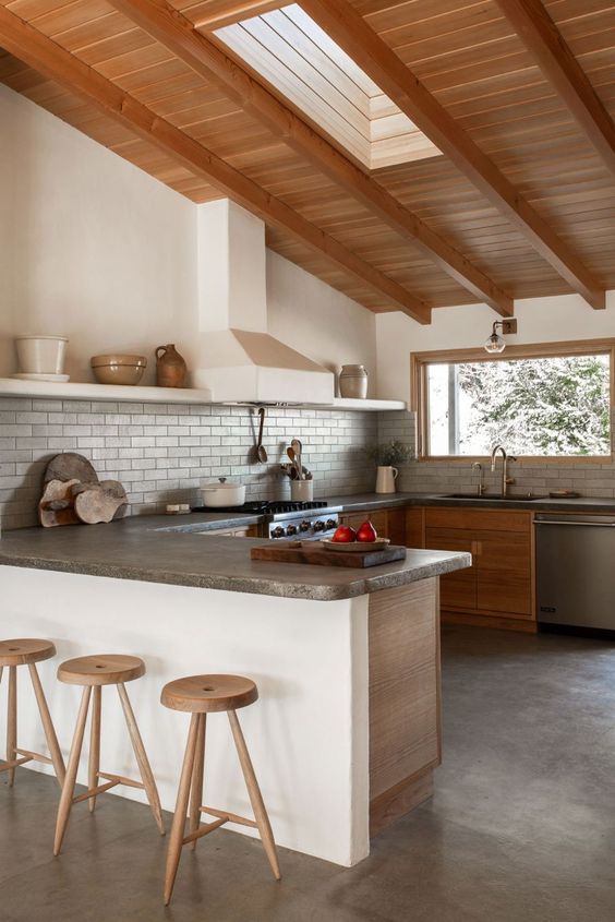 a rustic kitchen with stained cabinets, concrete countertops and a grey tile backsplash plus wooden beams on the ceiling