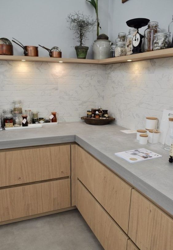 a stylish contemporary kitchen with light stained cabinets, concrete countertops, a corner wooden shelf with lights and a white marble tile backsplash