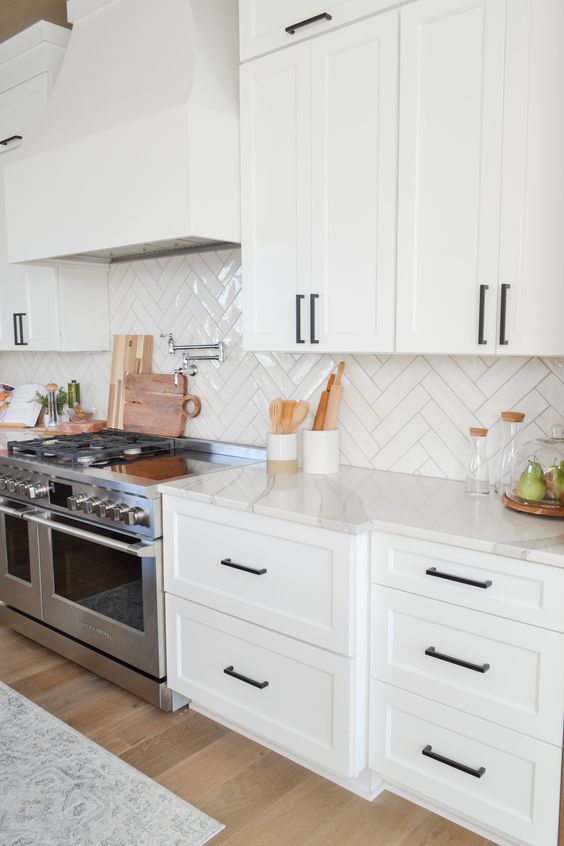 a stylish white farmhouse kitchen with a glossy white herringbone backsplash and black handles is a beautiful and chic space